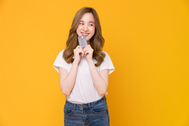 欢快美丽的亚洲女人在白色t恤和持有模型信用卡在黄色的背景。图片下载