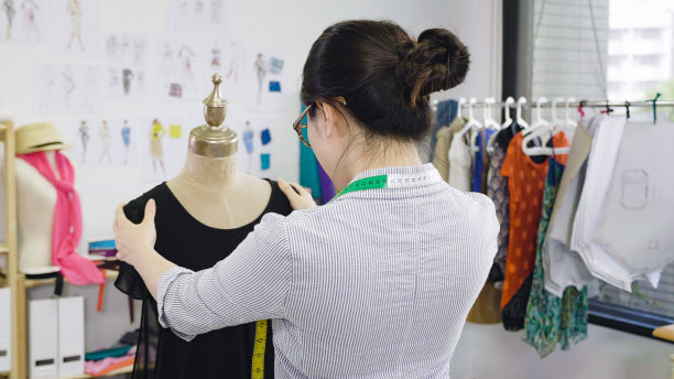 亚洲中国时尚设计师时尚展厅概念的后视图。年轻的女裁缝在工作室里固定假人的衣服。女裁缝工人在车间单独与新收集的人体模型。图片下载