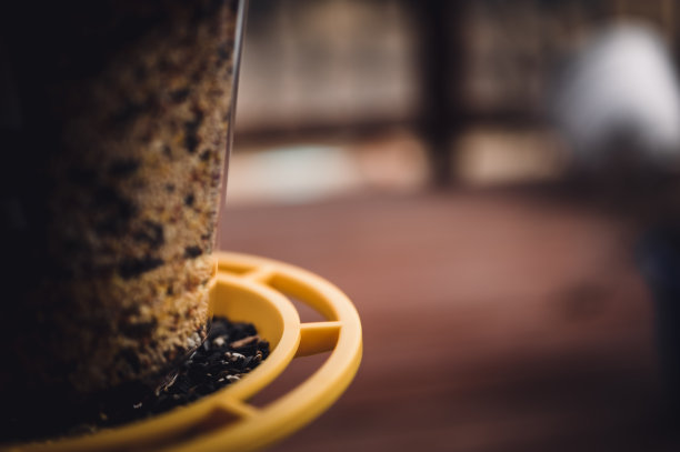 选择性集中于鸟食器与混合种子。模糊背景中的住宅木制门廊。图片下载