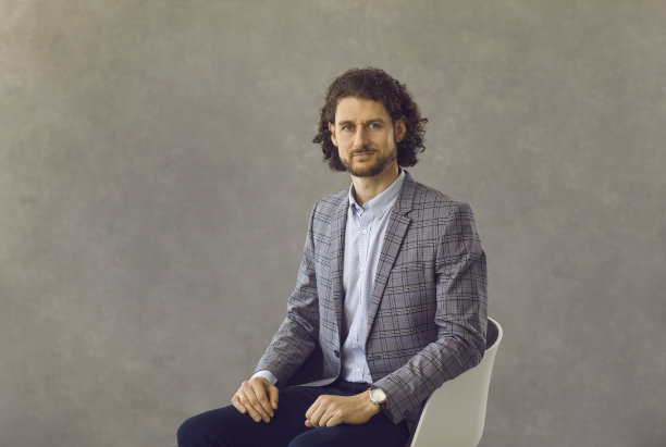 一个严肃的白人商人坐在灰色背景的椅子上的肖像。图片下载