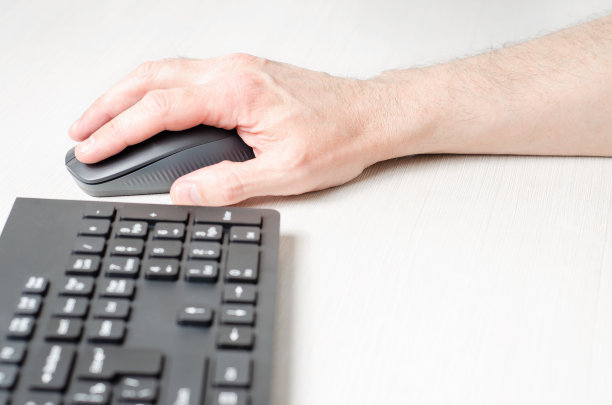 一个男人手里的电脑鼠标和一个黑色的键盘。白色背景。图片下载