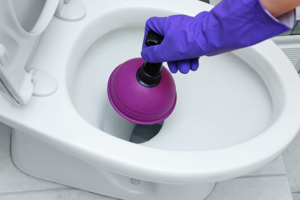 一只手戴着防护手套，用柱塞清洁马桶里的堵塞物。图片下载