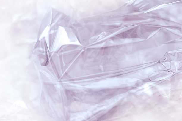 紫色背景上的透明塑料玻璃纸包装的纹理。塑料表面起皱撕裂，形成抽象图案。图片下载