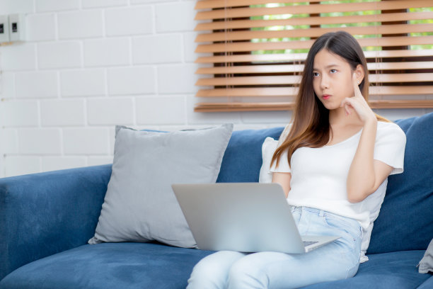 年轻的亚洲女性在家里沙发上的笔记本电脑上工作沮丧和无聊，自由职业的女孩不开心和疲惫与不成功，心烦问题，失败和错误，商业概念。图片下载