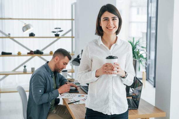 女人站在男人前面，男人坐在桌子旁边。两个设计师一起在办公室工作图片下载