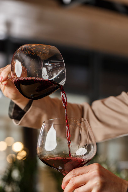 男性手拿着漂亮的透明高脚杯，盛勃艮第葡萄酒，红葡萄酒从另一个高脚杯倒进图片下载