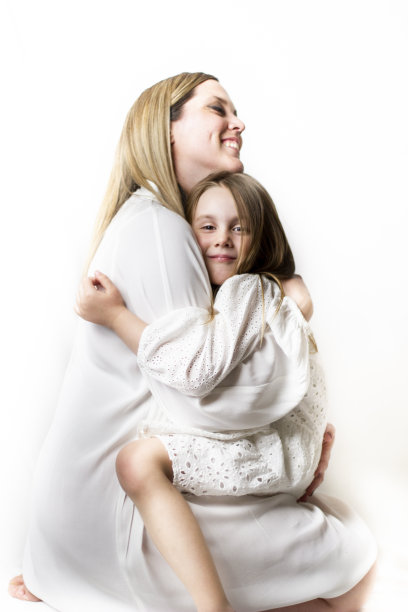 白色背景下，穿着白色衣服的蓝色母亲和蓝色女儿的温柔拥抱。幸福的家庭生活。影棚拍摄。股票的照片。图片下载
