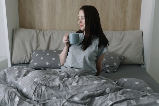 早晨，舒适，舒适的家庭概念——一个年轻的女人在家里的床上喝着咖啡或可可图片下载