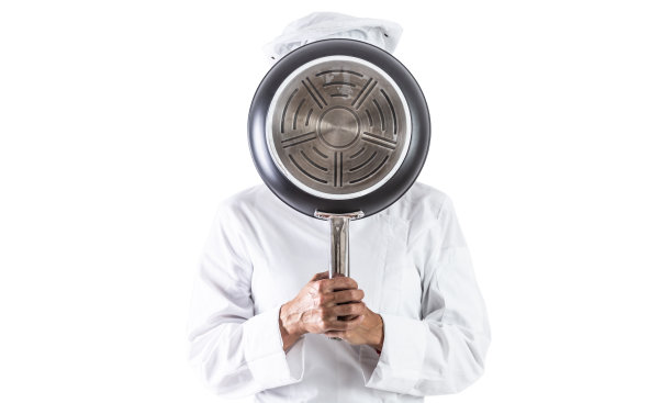 一个厨师在用煎锅盖住他的脸-孤立的白色。图片下载