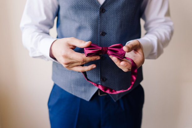 穿着蓝色西装和白色衬衫的男子手里拿着一个红色的领结。图片下载