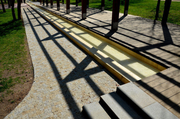 在公园的长廊上，一条人工小溪在斜坡上的水沟上下陷。水流通过水泵上下楼梯，瀑布瀑布的楼梯。米色池塘和木桥图片下载