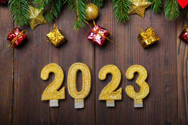 2023年新年快乐贺卡。木制背景上的蜡烛数字和布局圣诞树，球，礼物。关闭和复制空间，选择焦点。图片下载