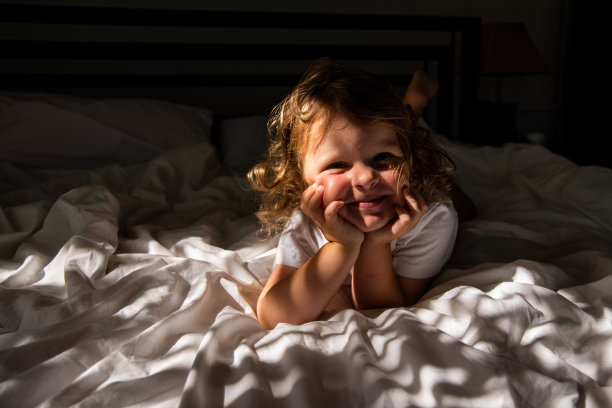 这孩子早晨很早就醒了。一个可爱的卷发女孩躺在床上晒太阳。新生儿窒息图片下载