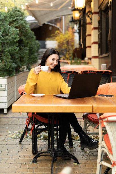 一位年轻美丽的女商人在秋天的户外咖啡馆里一边喝着咖啡，一边用笔记本电脑工作，图片下载