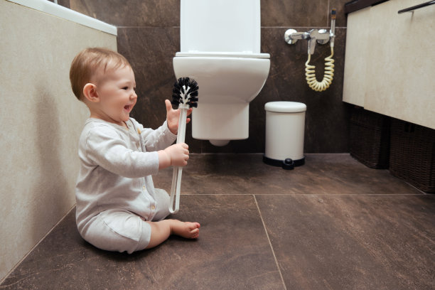 快乐的蹒跚学步的小男孩正在厕所里玩刷子。一个微笑的孩子在米色浴室的棕色地板上玩耍图片下载