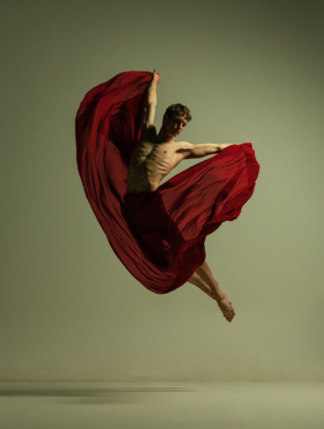 一个年轻的肌肉男，灵活的芭蕾舞演员在行动与红色织物，布孤立在橄榄色的背景。戏剧，情感，优雅，艺术，美的概念。图片下载