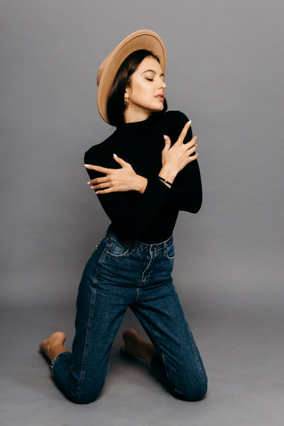 漂亮的女孩穿着黑色紧身套装，牛仔裤和草帽，孤立在灰色背景图片下载