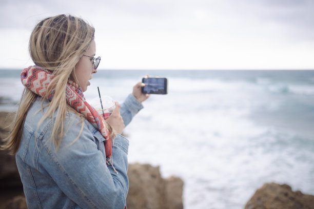 一名妇女用手机拍摄大海。图片下载