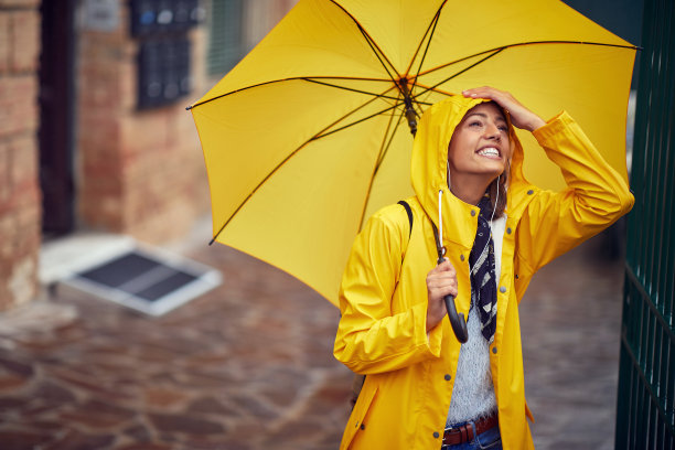 一个年轻开朗的女人，穿着黄色的雨衣和雨伞，在一个雨天的城市散步，心情很好。走,雨,城市图片下载