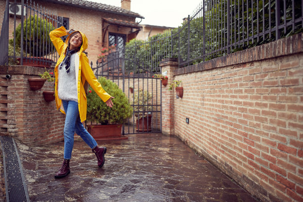 一个穿着黄色雨衣的年轻快乐的女人在雨天散步时摆姿势拍照。走,雨,城市图片下载
