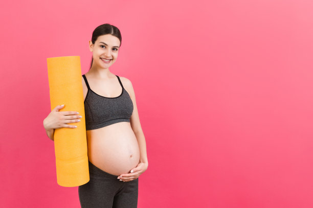 抱着瑜伽垫的怀孕女孩站在彩色背景上。工作室拍摄，设计的自由空间图片下载