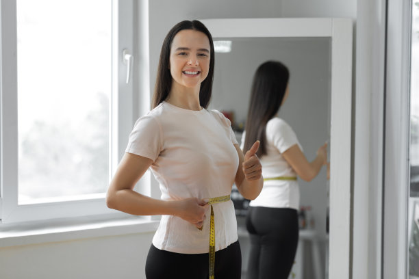 幸福的女人在镜子前用带子量腰围图片下载