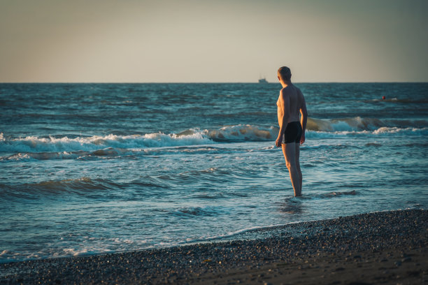 快乐的人穿着泳裤站在海边日落前享受生活。电影风格的照片。海边度假图片下载