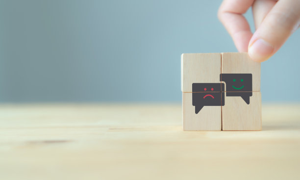 消费者反馈的概念。客户满意度评估，以改进和发展产品和服务。以客户为中心。手把木制立方体与“微笑”“悲伤”图标的灰色背景，复制空间图片下载