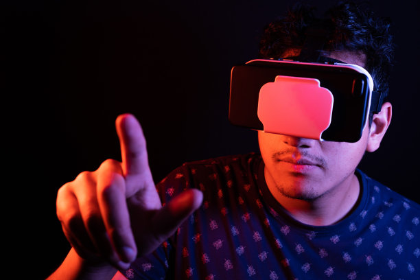 年轻的拉丁男子使用虚拟现实VR头盔3D眼镜，伸出手指触摸东西。黑暗的背景。低调图片下载