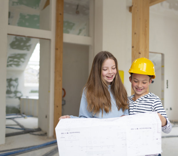 弟弟和妹妹在他们的新房间阁楼公寓的施工现场，带着平面图和黄色头盔，检查进度图片下载