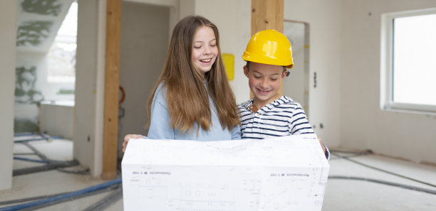 弟弟和妹妹在他们的新房间阁楼公寓的施工现场，带着平面图和黄色头盔，检查进度图片下载