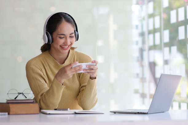 快乐的女人使用手机玩游戏在家庭办公室和聊天的朋友通过视频电话。图片下载