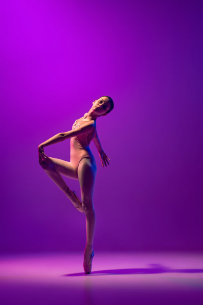 一个灵活的年轻女性芭蕾舞演员，青少年在舞台服装和尖跳舞孤立的紫色背景在霓虹灯。艺术，优雅，美丽，芭蕾学校的概念图片下载