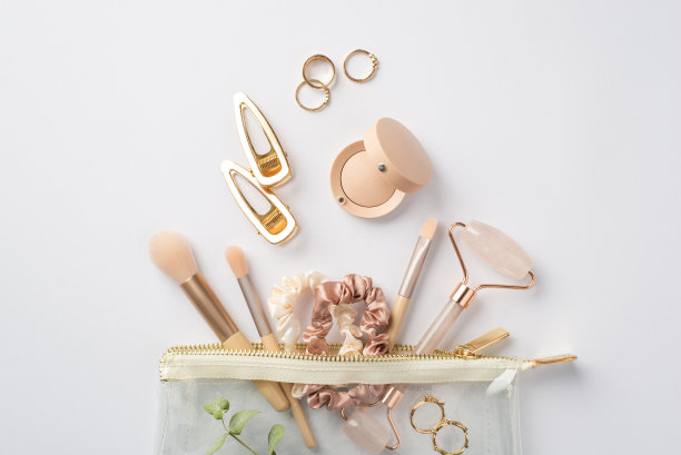 顶部视图照片的发夹玫瑰石英辊金戒指，化妆刷，发圈和眼影从透明化妆品袋和桉树枝上孤立的白色背景图片下载