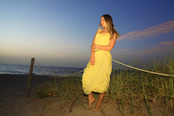 日出时沙滩上穿着黄色连衣裙的美丽年轻金发女子图片下载