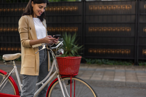 时髦的年轻女子在城市骑自行车时使用智能手机图片下载