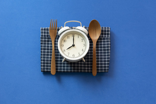 食物时钟勺子和叉子，健康的食物早餐概念在蓝色的桌子背景图片下载