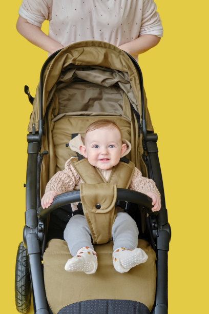 母亲和快乐的男婴在黄色背景的儿童车上，八个月大图片下载