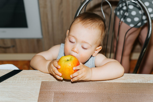 可爱的白人小男孩闭着眼睛坐在厨房里吃苹果，室内。有趣的孩子的肖像在桌子上的水果。儿童健康食品图片下载