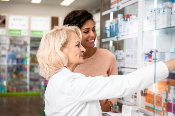 高级药剂师在药店向年轻女性顾客销售药品。图片下载