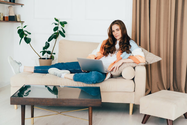 有思想的年轻女人在沙发上放松着手提电脑。图片下载