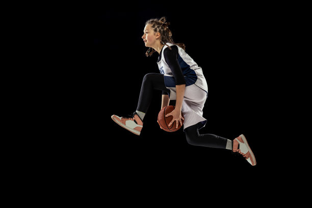 动态肖像十几岁的女孩，篮球运动员训练，跳跃与球孤立在黑色工作室背景。专业的运动图片下载