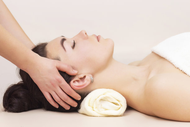 在水疗沙龙为一个女孩做头部和颞部按摩。保健按摩的概念。光背景。图片下载