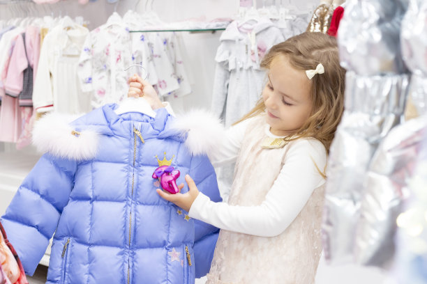 购物。折扣。小女孩购物狂。在精品店的试衣间里，一个女孩正在试穿一件粉红色的漂亮衣服。图片下载