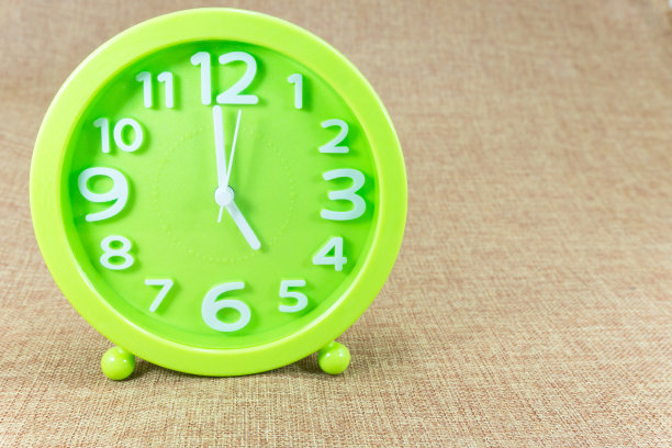 绿色闹钟在棕色麻布背景显示五点或五点。图片下载