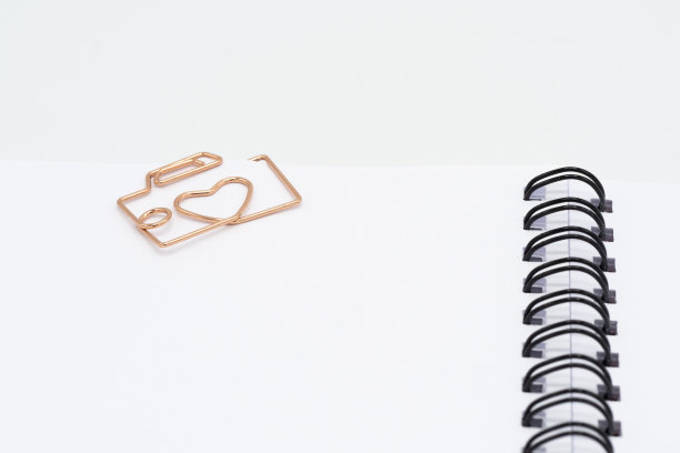 回形针形状相机与心在螺旋笔记本上的白色背景图片下载