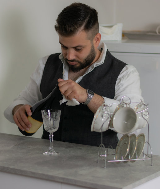 年轻人在家里的厨房里，倒了一些红酒来放松一整天的工作。图片下载