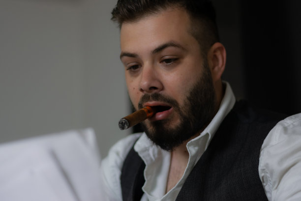 商人一边在办公室工作，一边翻阅文件，一边抽雪茄，一边思考他的下一步，一边寻找问题的解决方案，在办公桌上的笔记本电脑上工作到很晚。图片下载