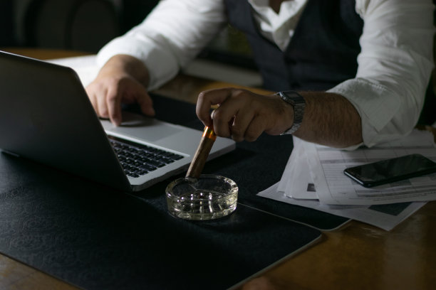 严肃英俊的商人，西装革履，倚在桌子上看图表。深夜工作的概念。工作到深夜为第二天做准备，完成他的工作。图片下载