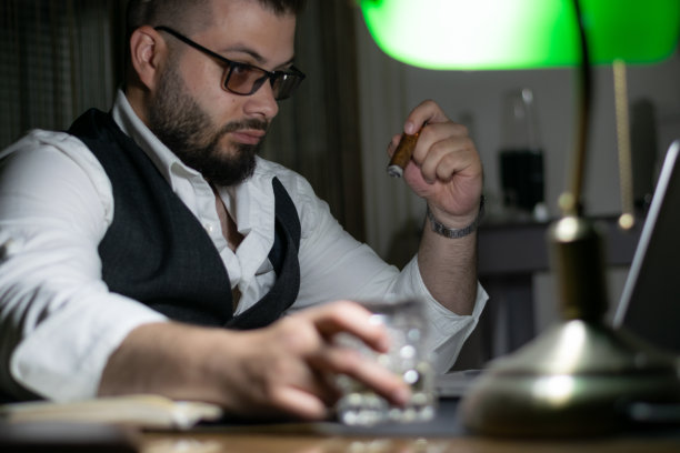 严肃英俊的商人，西装革履，倚在桌子上看图表。深夜工作的概念。工作到深夜为第二天做准备，完成他的工作。图片下载